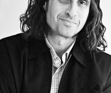 Geoff Siegel portrait, suit jacket, crossed arms, long wavy hair, closed mouth smile