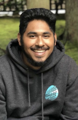 Photo of Ismael Velasquez, smiling, dark hair and small beard, grey hoodie with Santa Cruz symbol, Latinx
