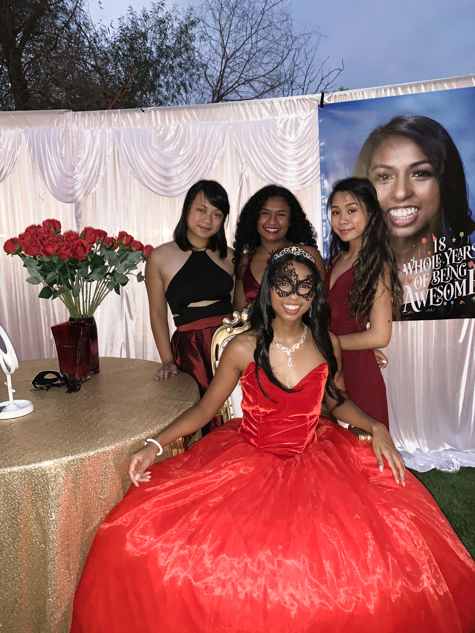 Katelyn Vengersammy in fancy red dress with three girl cousins and red roses behind her for Debut party.