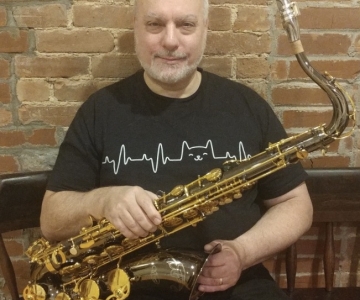 Norbert Stachel with saxophone, sitting white beard, small smile