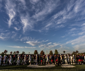 Sunny sky and football players lined up in distance, cloud patterns in wavy shapes