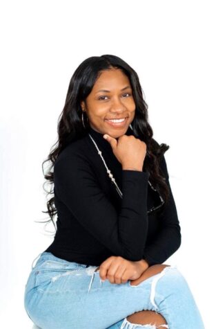 Vontress Ortega smiling with long black hair and legs crossed