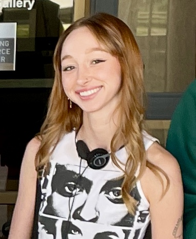 Mckenna Ingram smiling with headphones around neck and teeshirt imprinted with black and white photos of faces looking out 