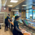 Subway store workers stand behind counter and take order to make sandwiches