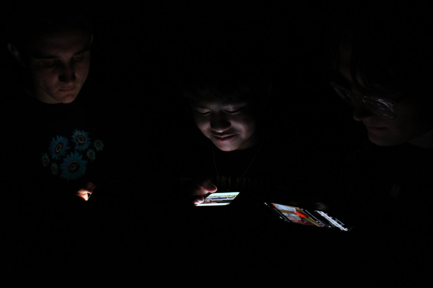 People look down on illuminated phones in a dark room