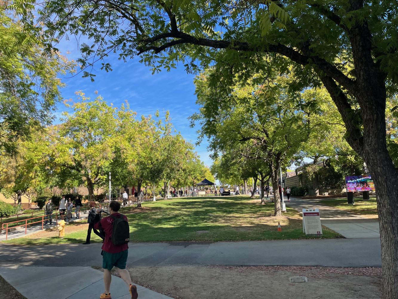 Rocklin campus quad with green grass and trees, person walking in foreground