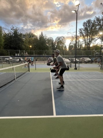 two people are standing at the kitchen line of a pickleball court, playing a game of pickleball