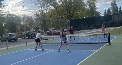 four people are standing on a pickleball court, two on each side, playing a game of pickleball