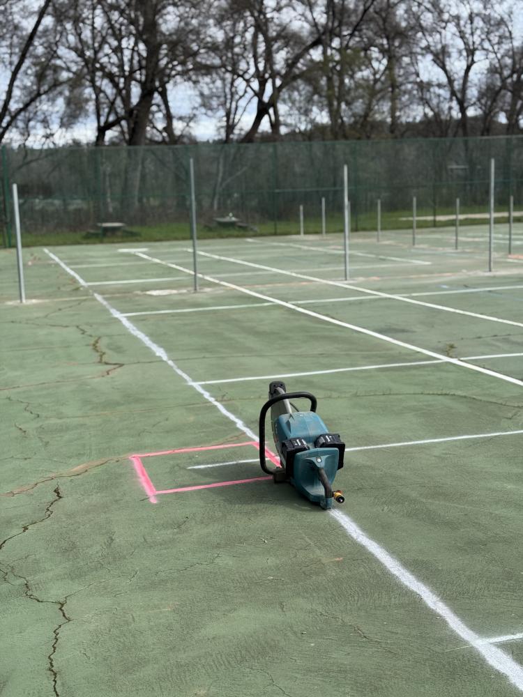 old tennis courts are spray painted with lines for making them into pickleball courts. posts in the ground for new fencing