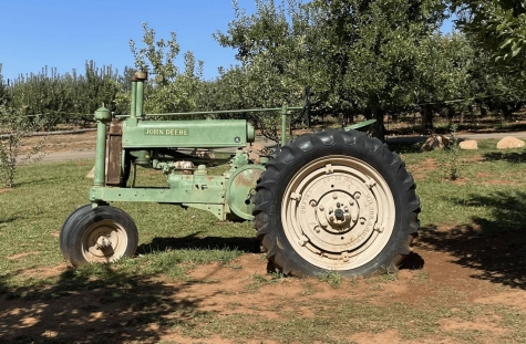 an old green tractor with large back wheels sitting on a grass and dirt open field