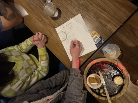 people filling in a trivia answer sheet at a wooden table with food and drink